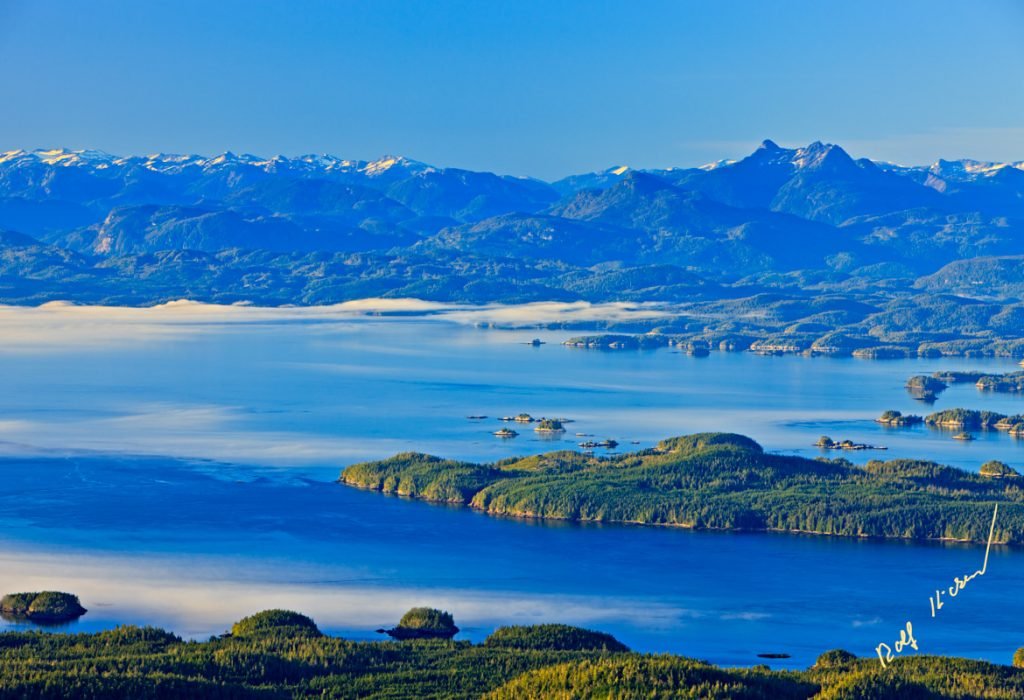 Aerial view over Johnstone Strait, Hanson Island, Blackfish Sound, Bold Head on Swanson Island, the White Cliff Islands towards Fife Sound and the British Columbia Coastal Mountains with Mount Stephens on the right, while fog is rolling in from Queen Charlotte Strait, First Nations Territory, Traditional Territories of the Kwakwaka'wakw People, British Columbia, Canada.⁠